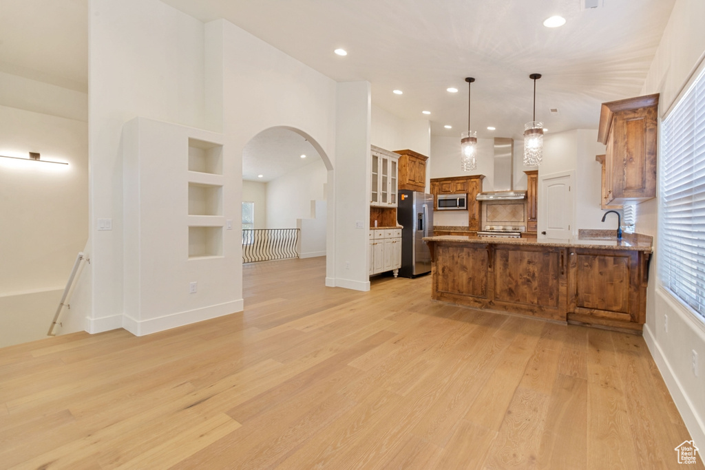 Kitchen featuring hanging light fixtures, wall chimney exhaust hood, built in shelves, appliances with stainless steel finishes, and kitchen peninsula