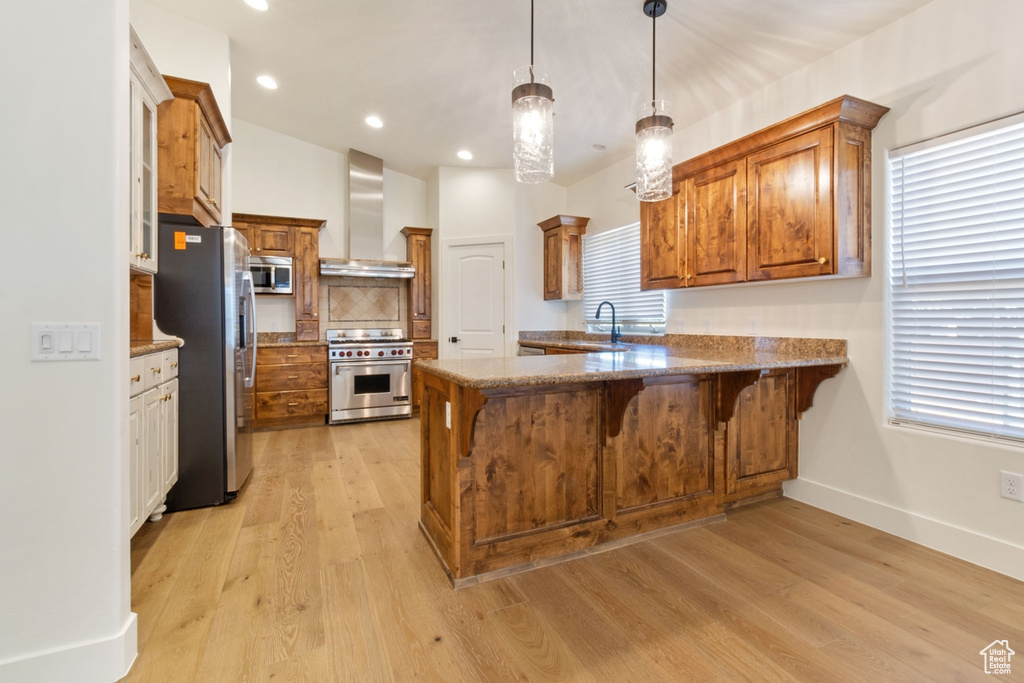 Kitchen with kitchen peninsula, appliances with stainless steel finishes, a breakfast bar, wall chimney range hood, and decorative light fixtures