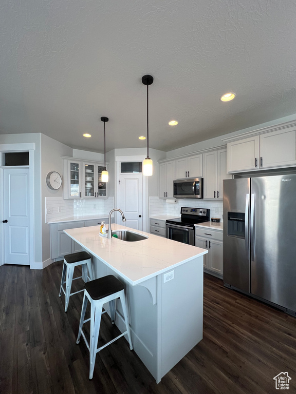 Kitchen with a kitchen island with sink, sink, hanging light fixtures, appliances with stainless steel finishes, and white cabinetry