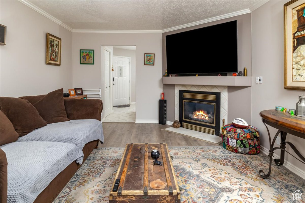 Living room featuring a textured ceiling, light hardwood / wood-style floors, ornamental molding, and a tiled fireplace