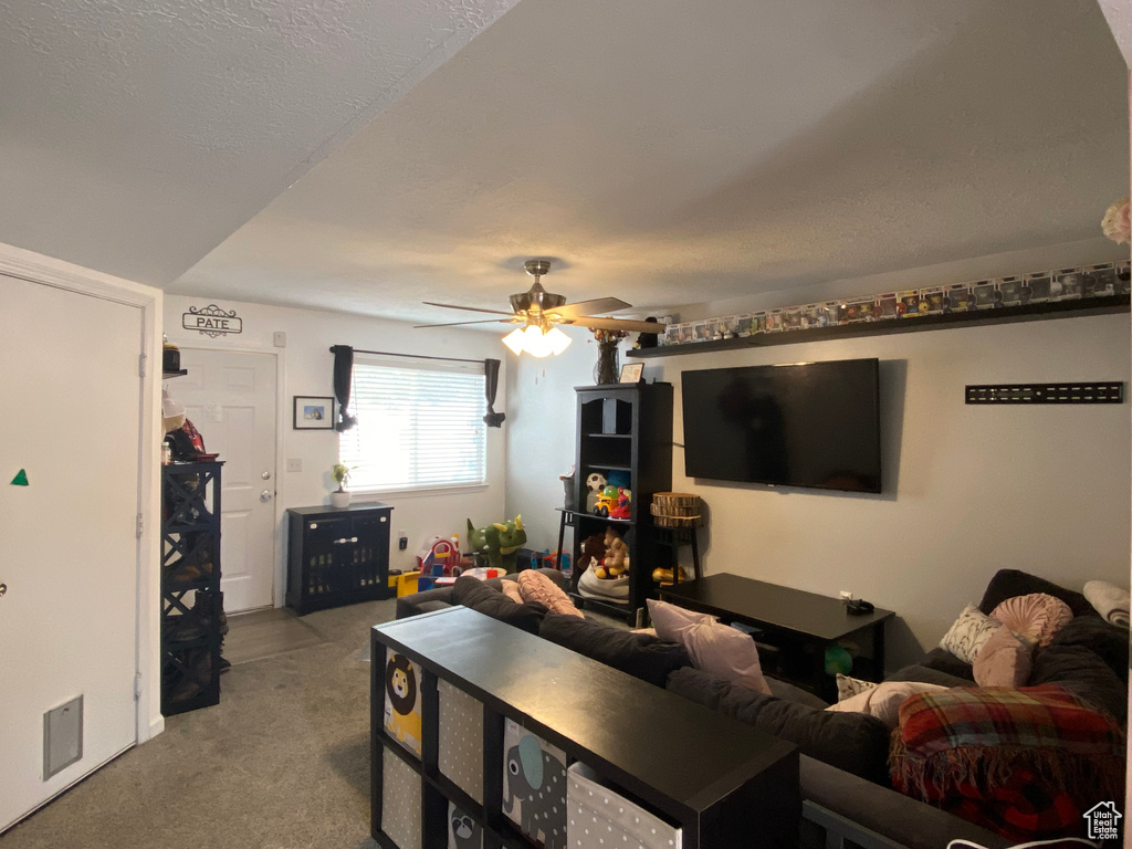 Carpeted living room featuring ceiling fan and a textured ceiling