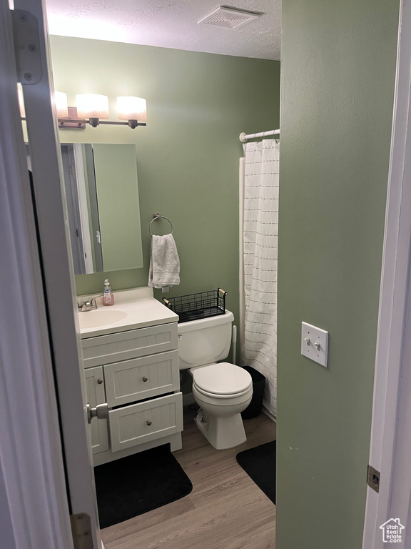 Bathroom with a textured ceiling, vanity, toilet, a shower with shower curtain, and hardwood / wood-style flooring
