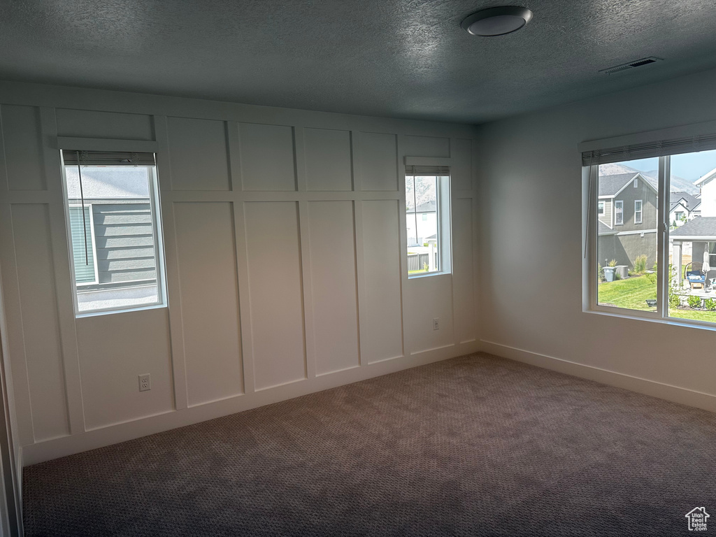 Carpeted empty room with a textured ceiling and baseboards