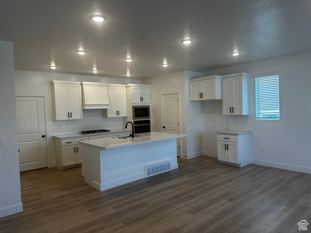 Kitchen featuring built in microwave, oven, gas stovetop, dark wood-style flooring, and a textured ceiling