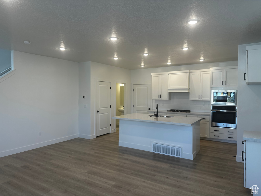 Kitchen featuring appliances with stainless steel finishes, dark wood-type flooring, white cabinets, light countertops, and recessed lighting