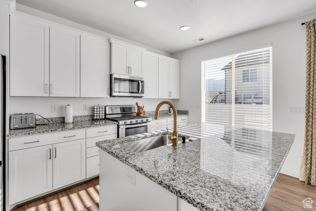 Kitchen featuring light stone counters, stainless steel appliances, a kitchen island with sink, sink, and white cabinets