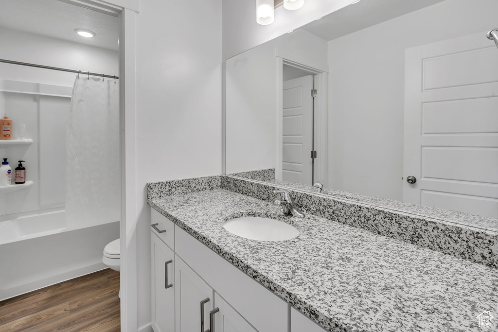 Full bathroom featuring hardwood / wood-style floors, vanity, shower / tub combo, and toilet