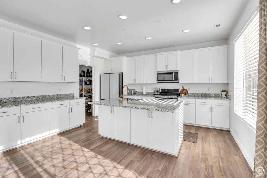 Kitchen featuring appliances with stainless steel finishes, white cabinetry, and light stone counters