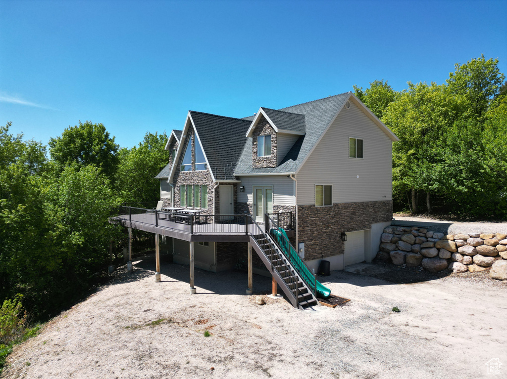 Back of property featuring stairway, stone siding, a wooden deck, a shingled roof, and an attached garage