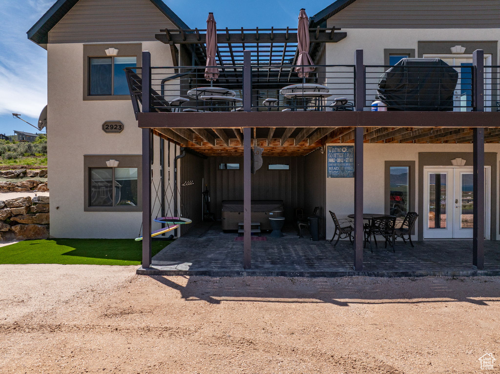 Rear view of house with a hot tub, french doors, stucco siding, a patio area, and a balcony