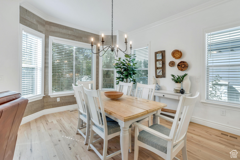 Dining area with an inviting chandelier, a healthy amount of sunlight, crown molding, and light hardwood / wood-style flooring