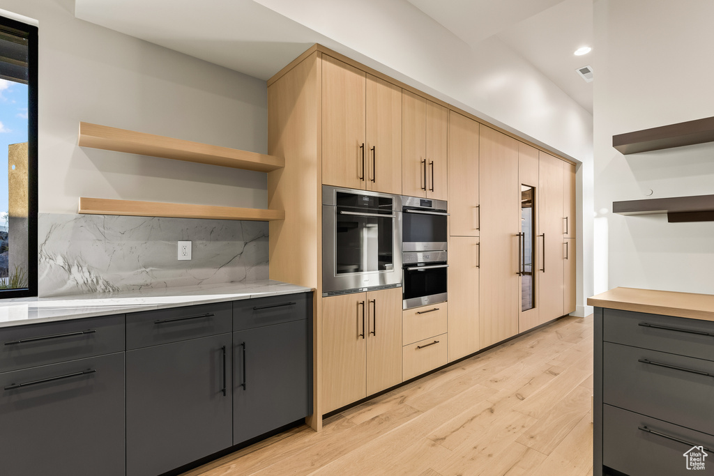 Kitchen with light brown cabinets, light hardwood / wood-style flooring, double oven, gray cabinets, and decorative backsplash