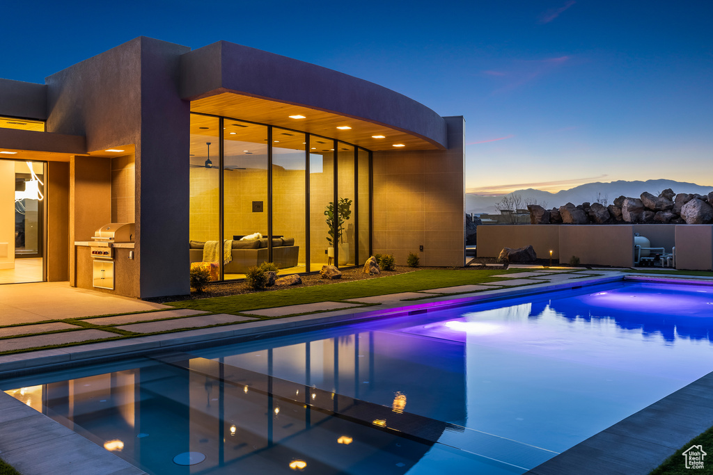 Pool at dusk featuring a mountain view, an outdoor kitchen, and a patio