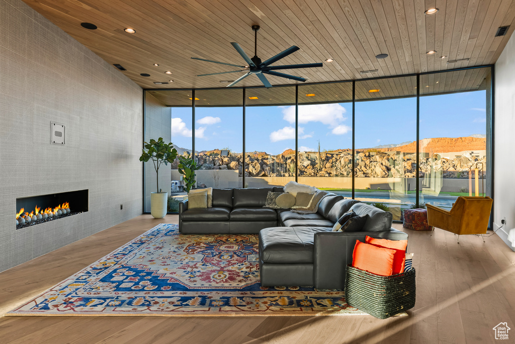 Living room with floor to ceiling windows, wood ceiling, a tiled fireplace, and light wood-type flooring