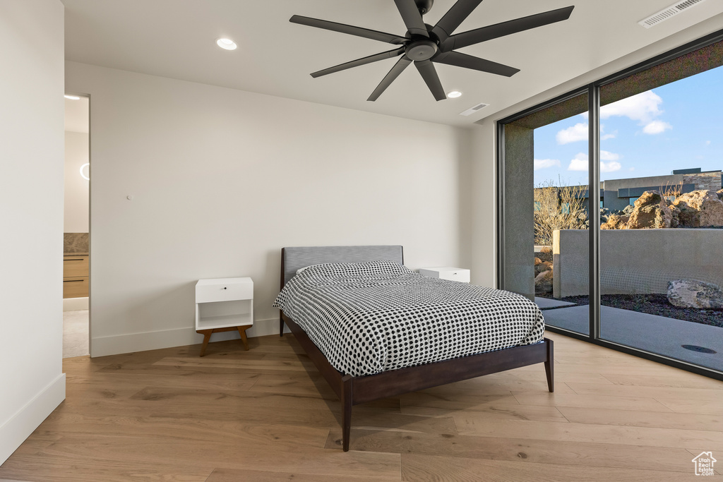 Bedroom with ensuite bathroom, expansive windows, access to outside, ceiling fan, and light hardwood / wood-style floors