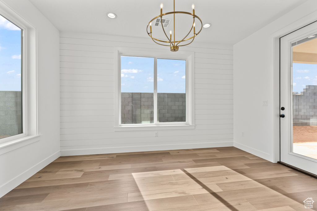 Unfurnished dining area with light hardwood / wood-style flooring, a notable chandelier, and wood walls