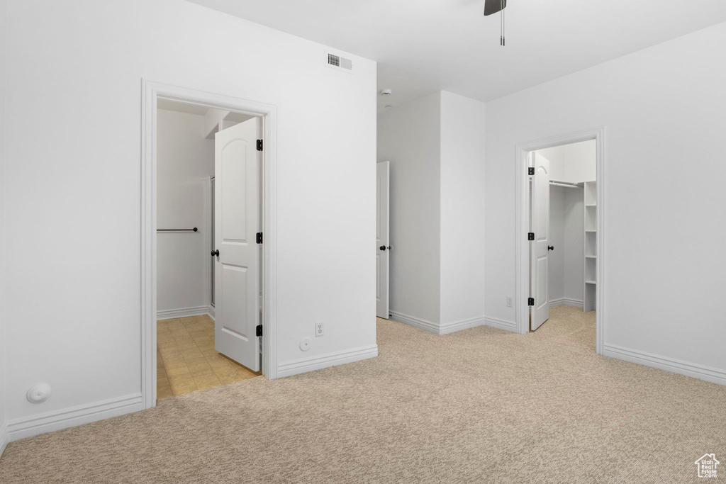 Unfurnished bedroom with a closet, light colored carpet, a spacious closet, and ceiling fan