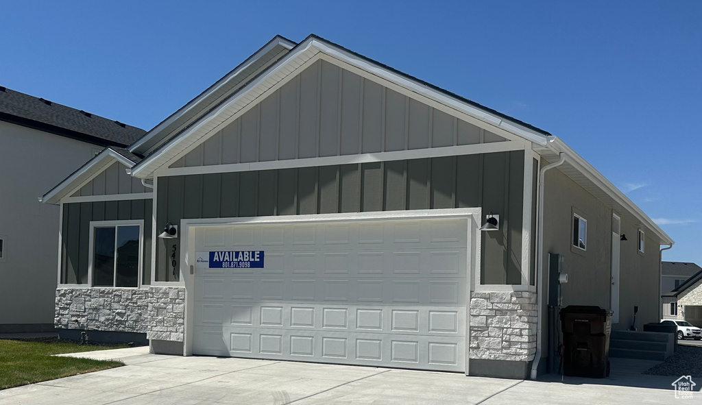 View of front of house with stone siding, board and batten siding, an attached garage, and concrete driveway