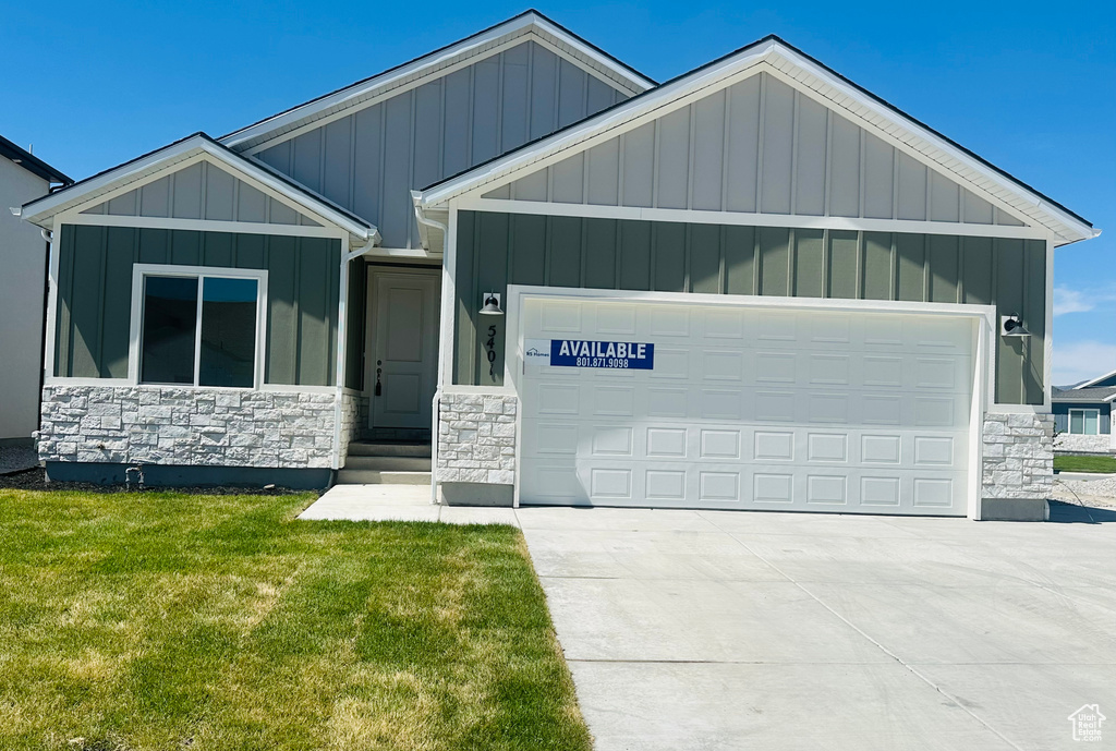 View of front of home with stone siding, an attached garage, board and batten siding, a front lawn, and driveway