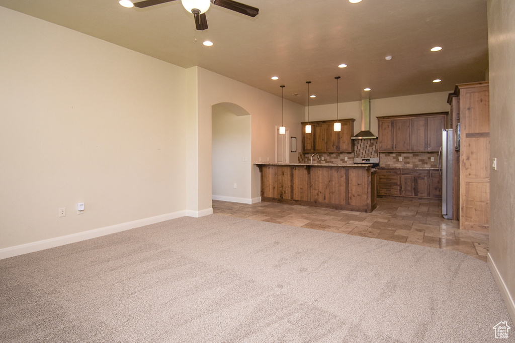 Kitchen with wall chimney range hood, hanging light fixtures, ceiling fan, tasteful backsplash, and light colored carpet