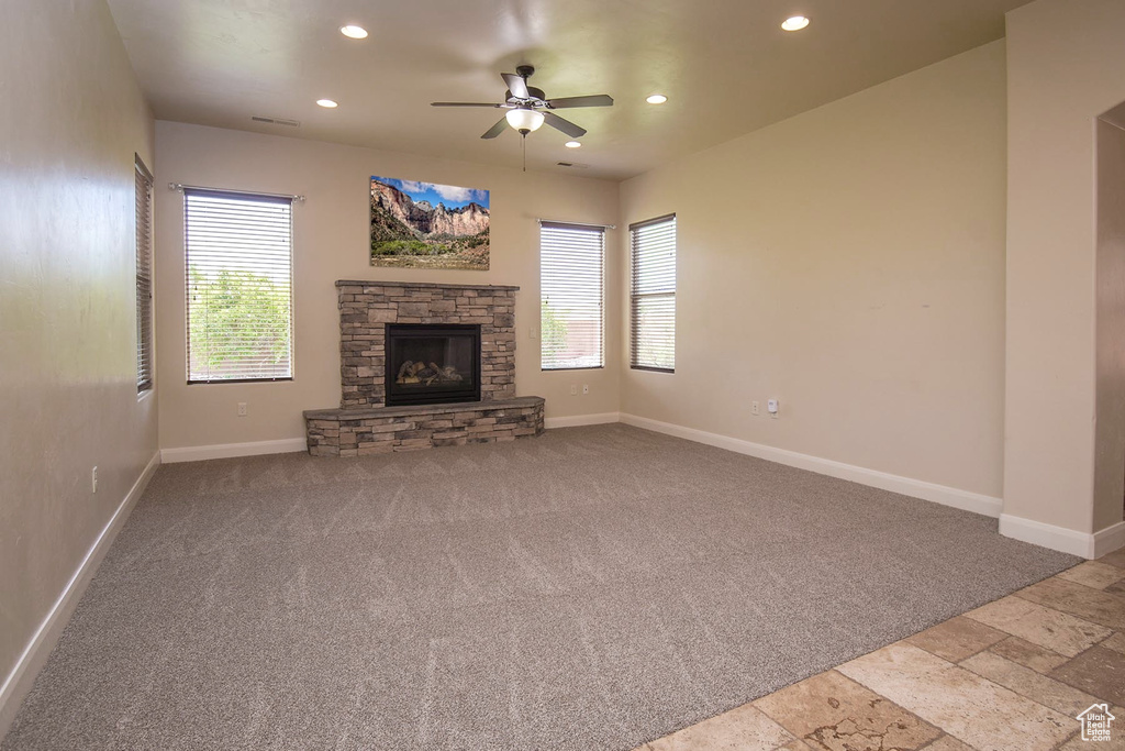 Unfurnished living room with ceiling fan and a stone fireplace