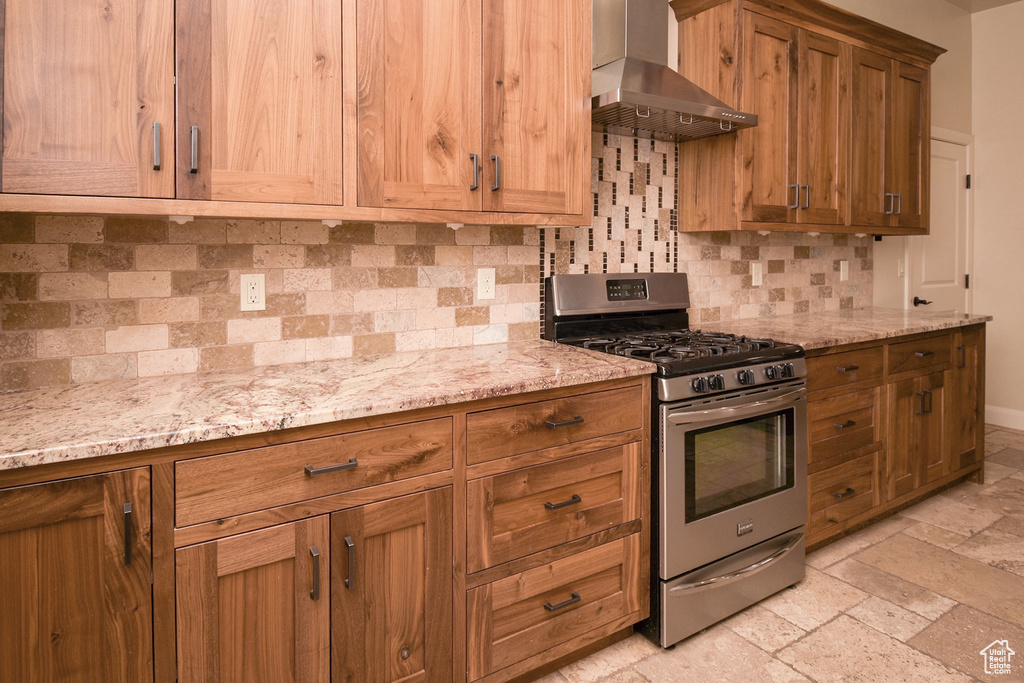 Kitchen featuring light stone countertops, wall chimney range hood, backsplash, and gas range