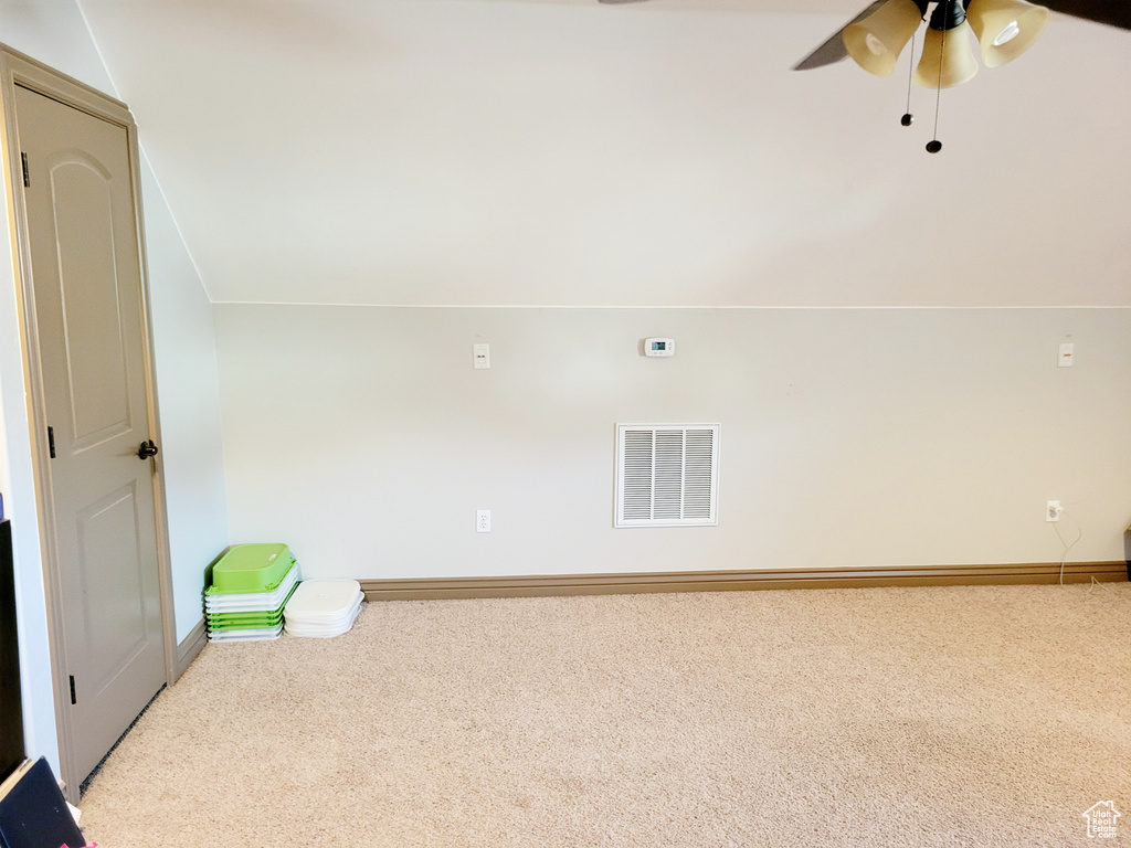 Empty room with light colored carpet, vaulted ceiling, and ceiling fan