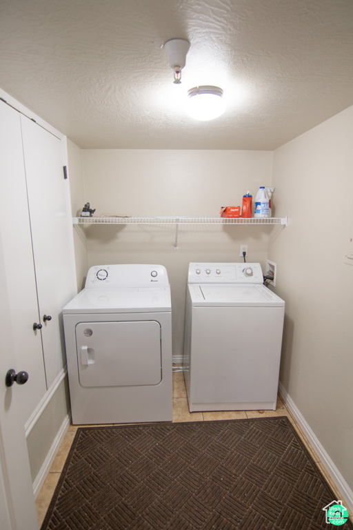 Laundry area with washing machine and clothes dryer, light tile patterned floors, and a textured ceiling