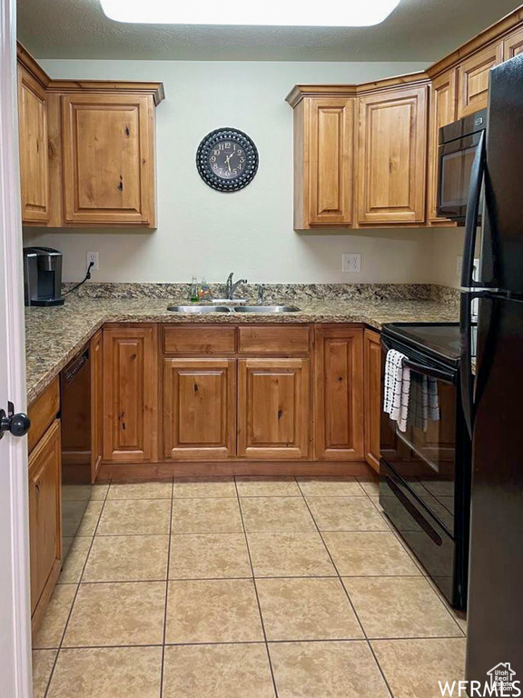 Kitchen featuring light stone countertops, sink, light tile patterned floors, and black appliances