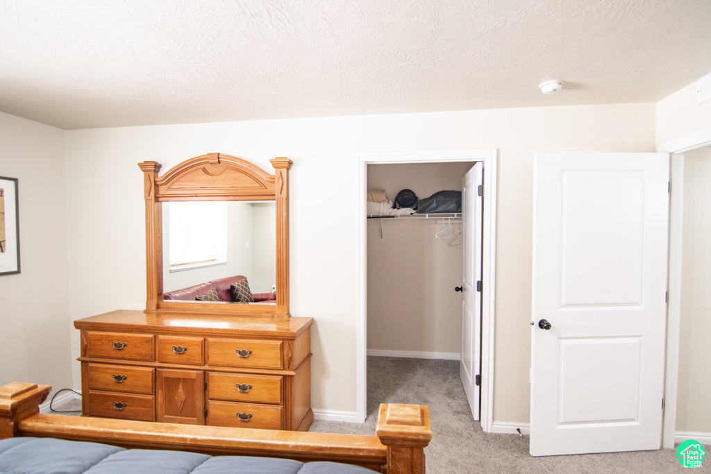 Bedroom with a walk in closet, light colored carpet, a closet, and a textured ceiling