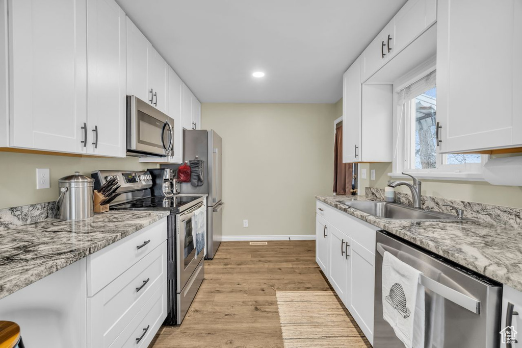 Kitchen with white cabinets, appliances with stainless steel finishes, light hardwood / wood-style floors, and sink