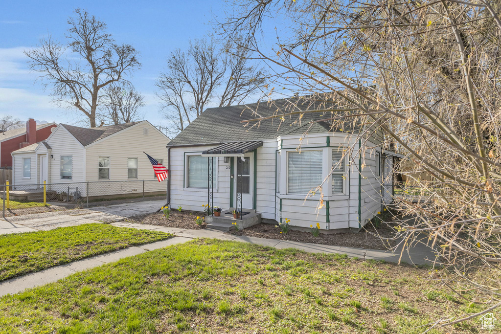 Bungalow-style house with a front yard, fence, and a shingled roof