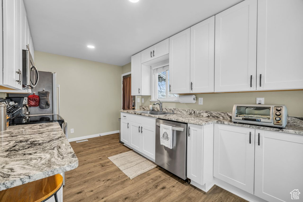 Kitchen featuring light stone countertops, stainless steel appliances, sink, white cabinets, and light hardwood / wood-style floors