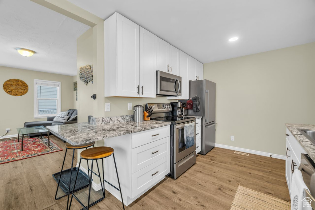 Kitchen with kitchen peninsula, appliances with stainless steel finishes, light wood-type flooring, a breakfast bar, and white cabinetry