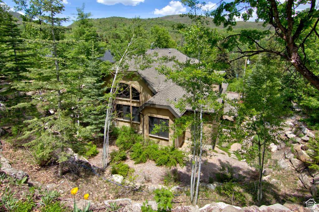 View of home\\\\\\\'s exterior featuring roof with shingles, stucco siding, and a forest view