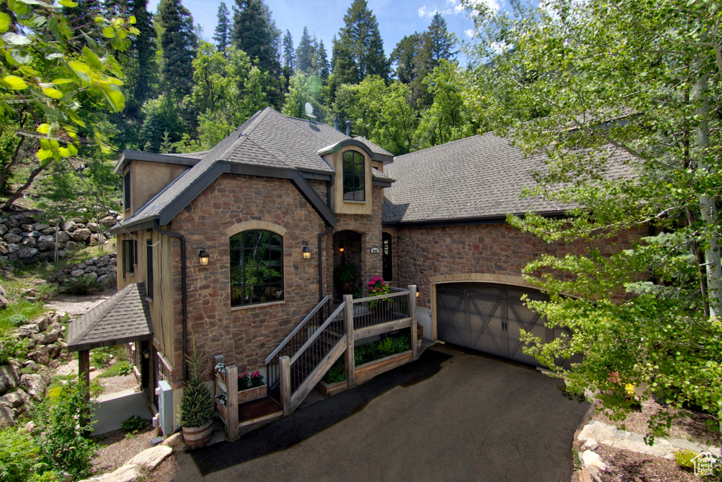 View of front of house with stone siding, a shingled roof, asphalt driveway, and an attached garage