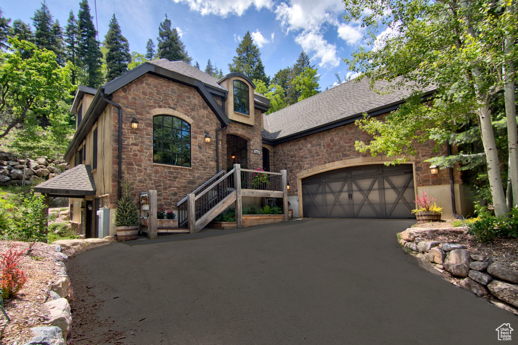 View of front facade featuring stone siding, a garage, asphalt driveway, and a shingled roof
