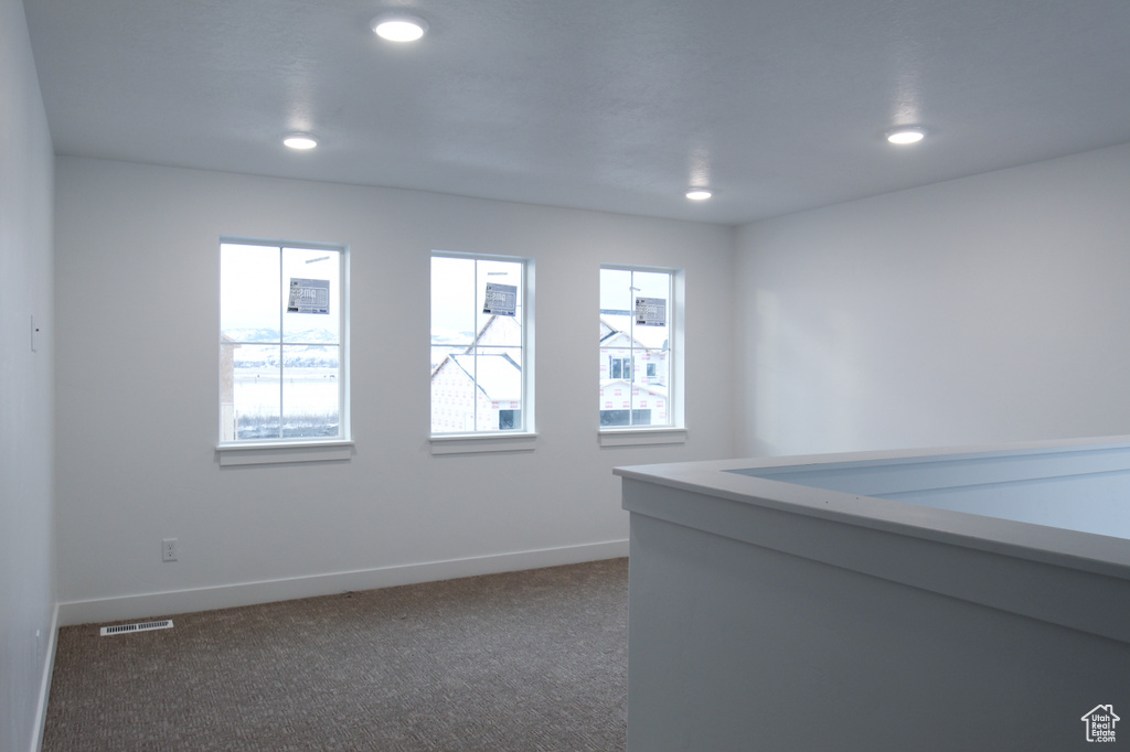 Empty room featuring dark carpet, baseboards, and recessed lighting