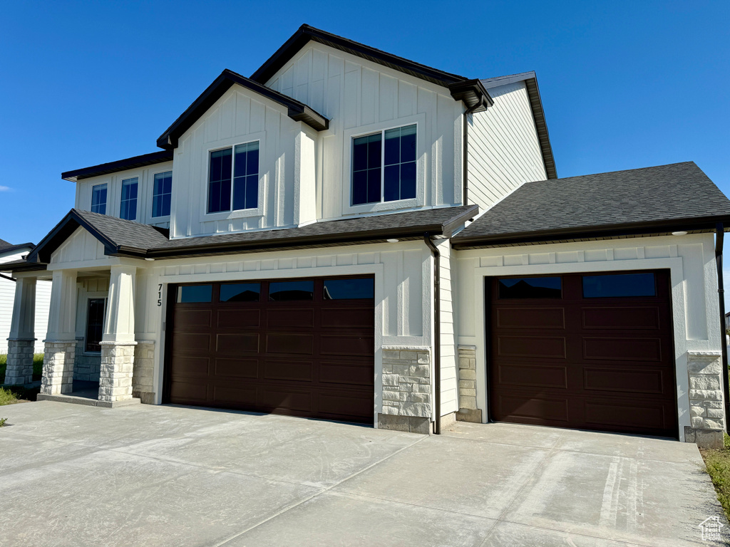 View of front of home featuring board and batten siding, stone siding, concrete driveway, an attached garage, and a shingled roof