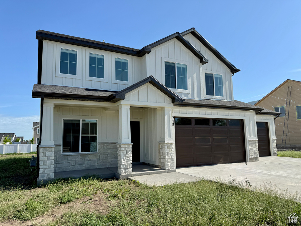 View of front of house with board and batten siding, stone siding, an attached garage, and concrete driveway