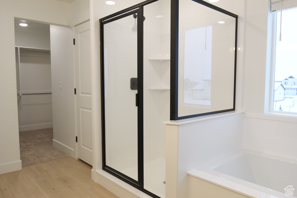 Bathroom with a stall shower, wood finished floors, a spacious closet, a garden tub, and recessed lighting