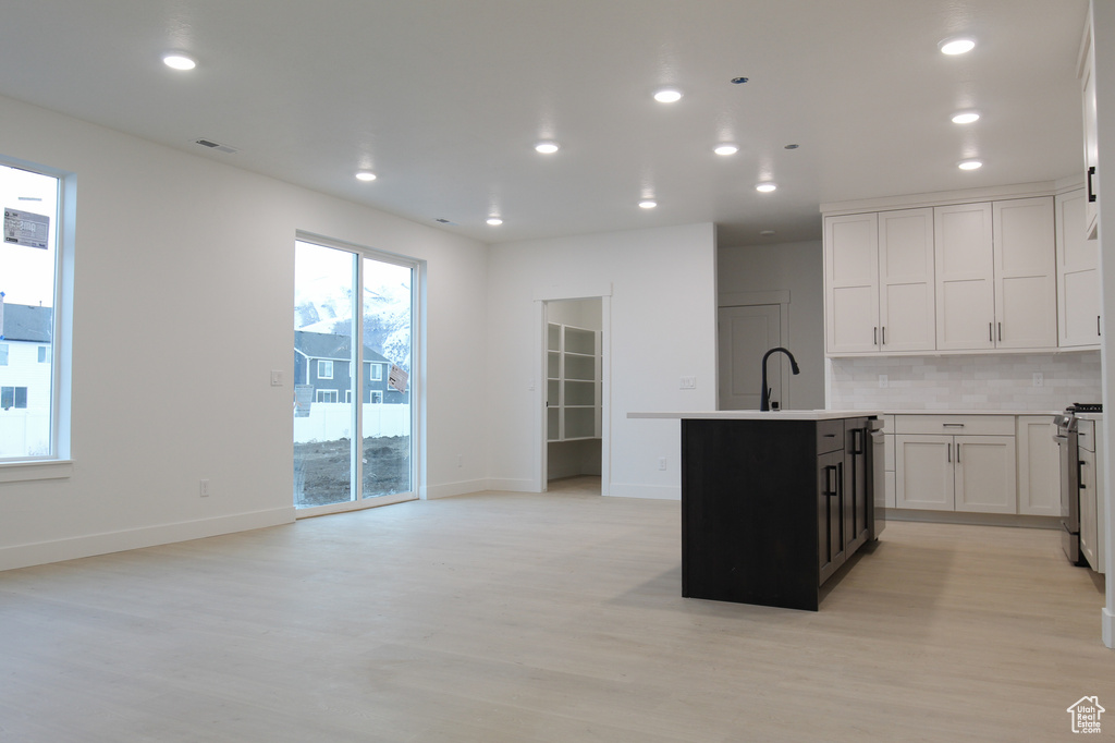 Kitchen with light wood-style floors, a center island with sink, stainless steel range with gas cooktop, tasteful backsplash, and recessed lighting