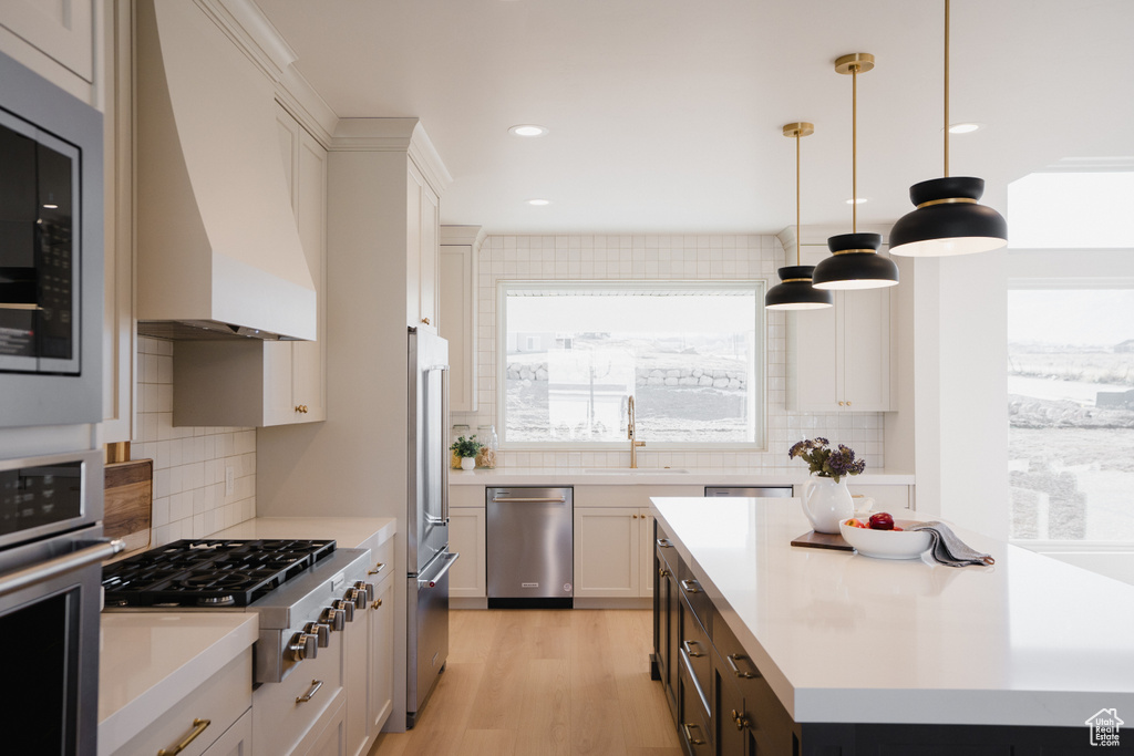 Kitchen with tasteful backsplash, custom range hood, stainless steel appliances, pendant lighting, and white cabinetry