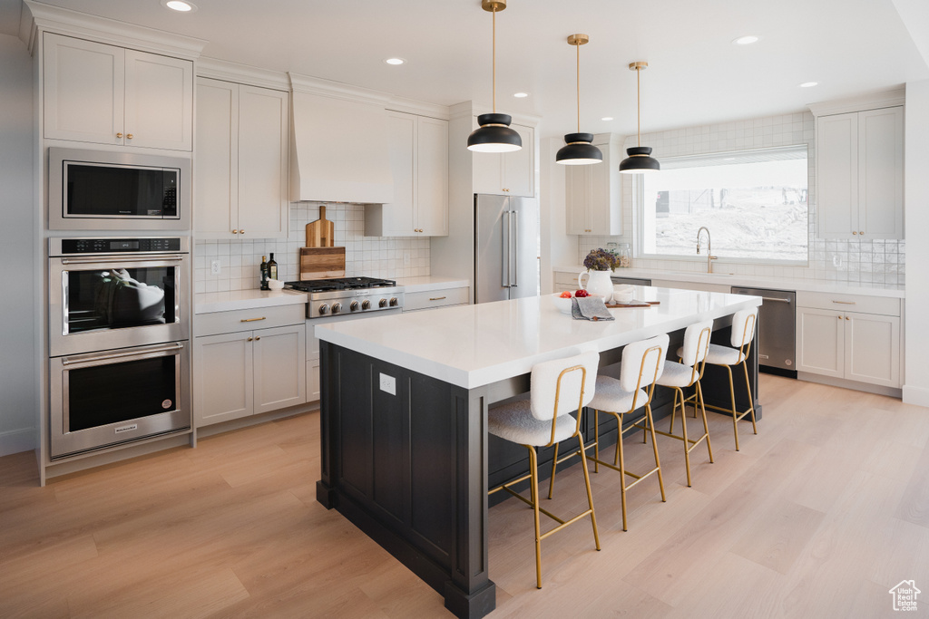 Kitchen with a breakfast bar, custom range hood, stainless steel appliances, white cabinets, and a kitchen island