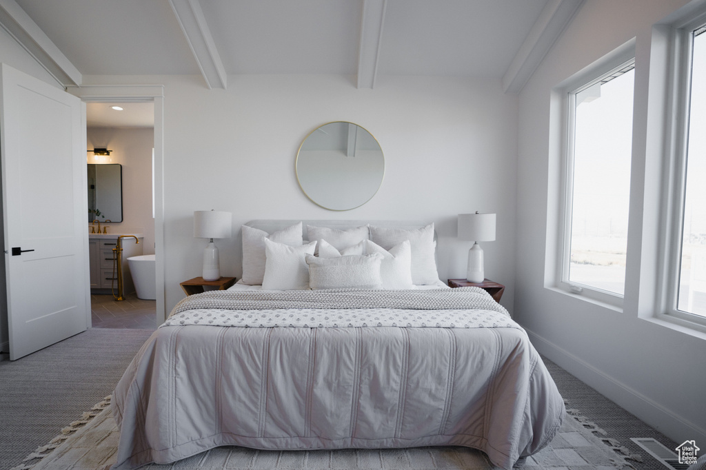 Bedroom with beam ceiling, light colored carpet, multiple windows, and ensuite bath