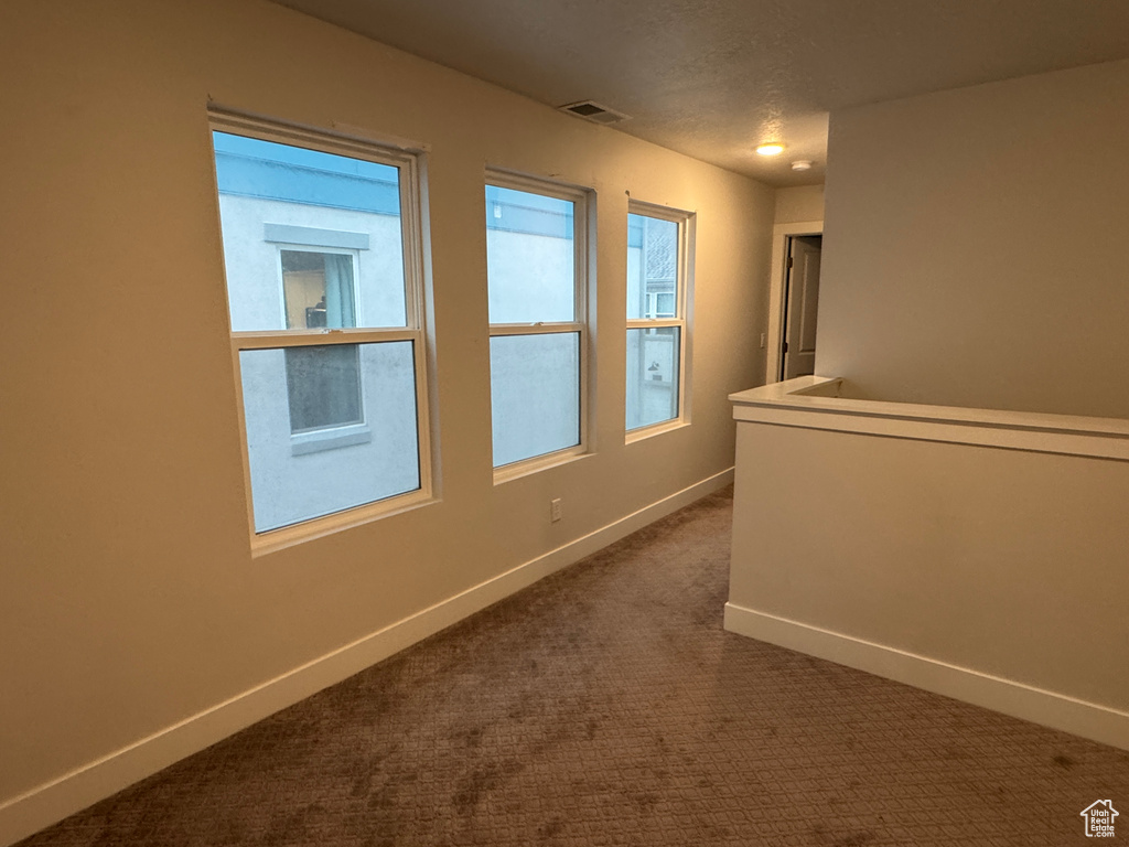Hallway featuring dark colored carpet and a textured ceiling