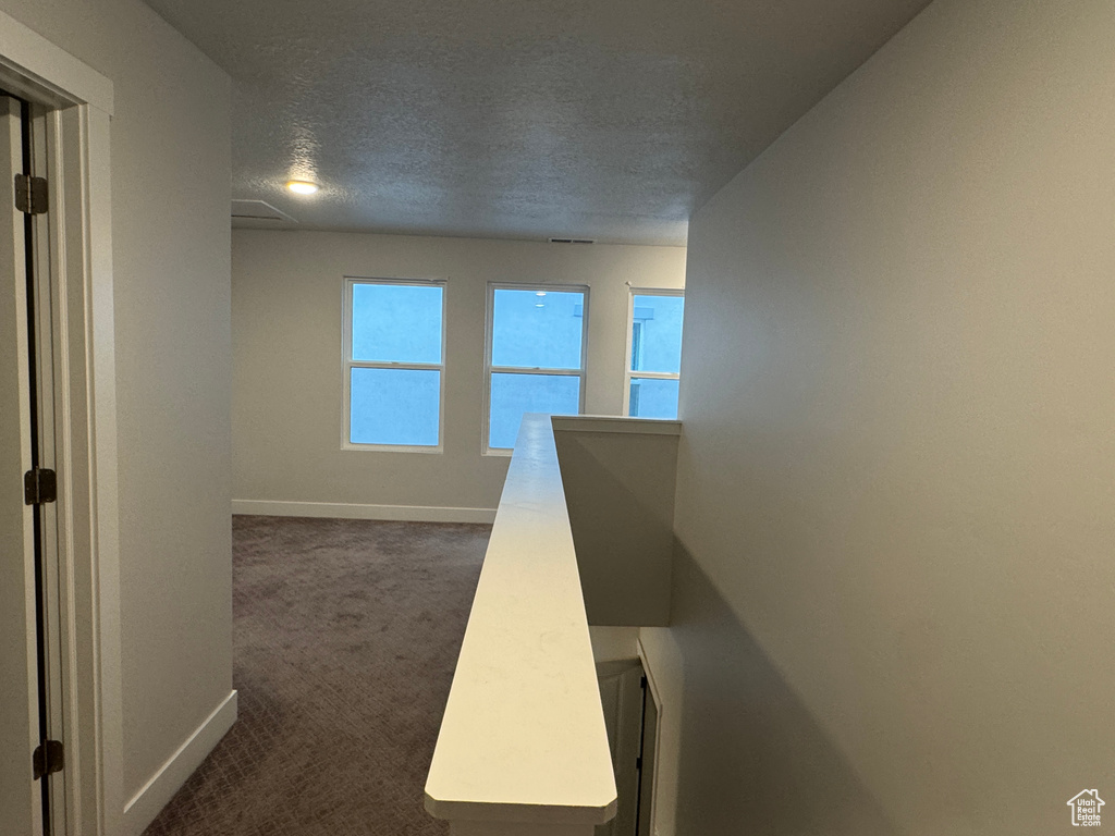 Hallway featuring dark colored carpet and a textured ceiling