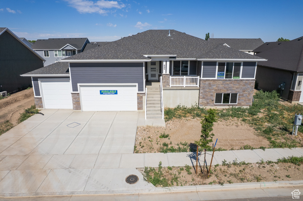 View of front facade featuring stone siding, a garage, covered porch, concrete driveway, and roof with shingles