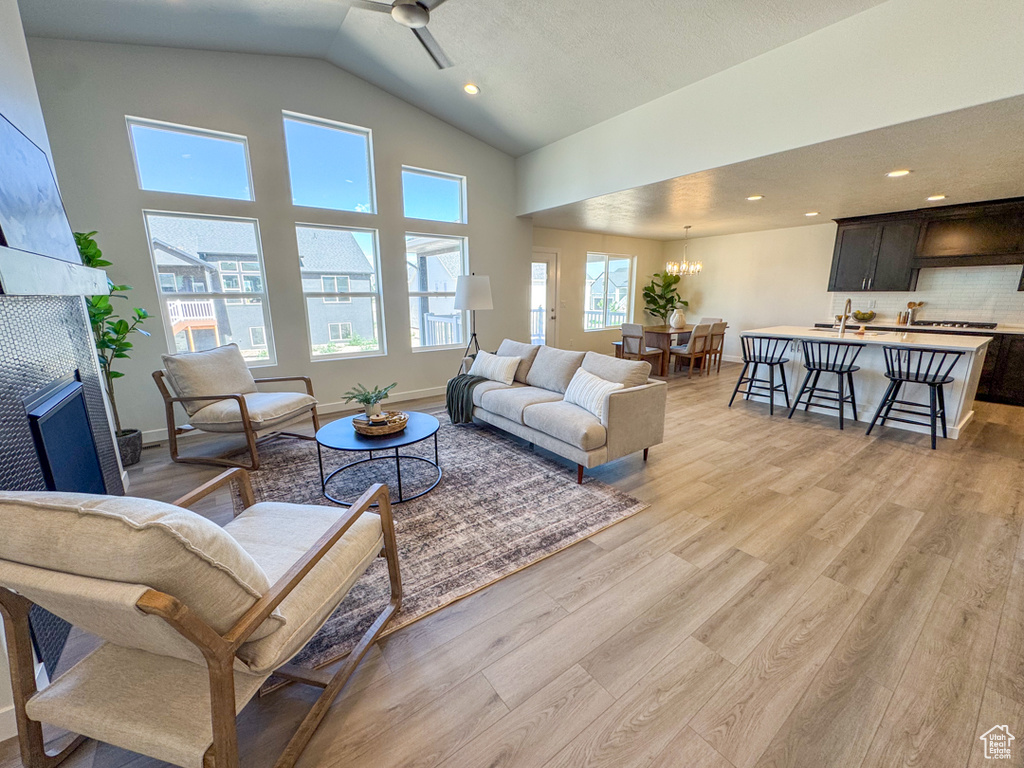 Living area with light wood-style flooring, a ceiling fan, recessed lighting, a chandelier, and high vaulted ceiling