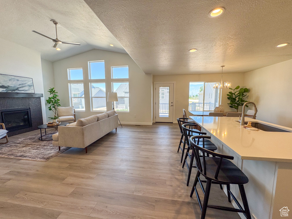 Living area featuring a textured ceiling, a fireplace, healthy amount of natural light, light wood-style floors, and vaulted ceiling